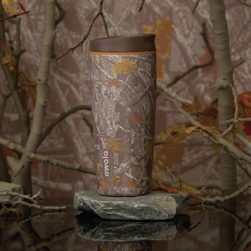 Owala SmoothSip Slider in Out of Sight, woodland camo patterned body in brown and tan with matching brown flip cap and carry loop, shown on a mossy rock against a forest backdrop